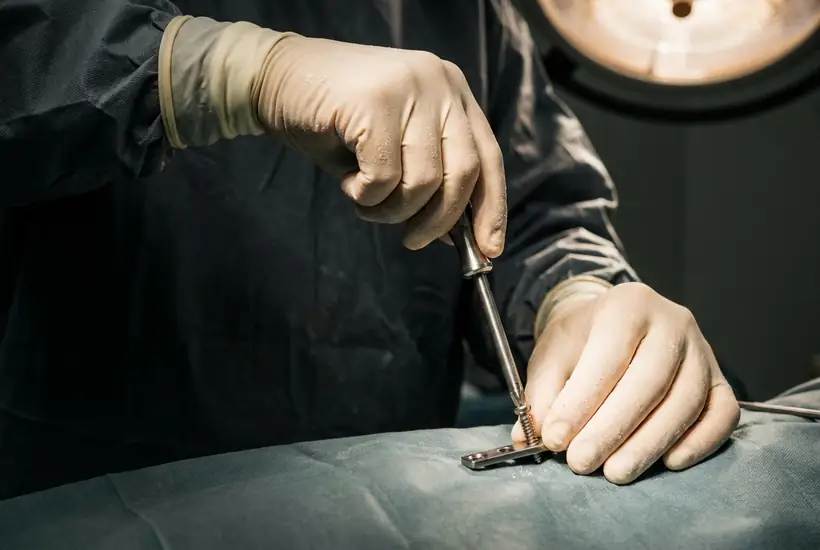Gloved surgeon hands securing a locking screw into an orthopaedic fixation plate