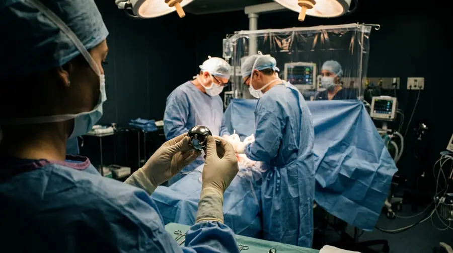 Scrub nurse presenting a bipolar hip prosthesis to the surgeon during hip fracture surgery